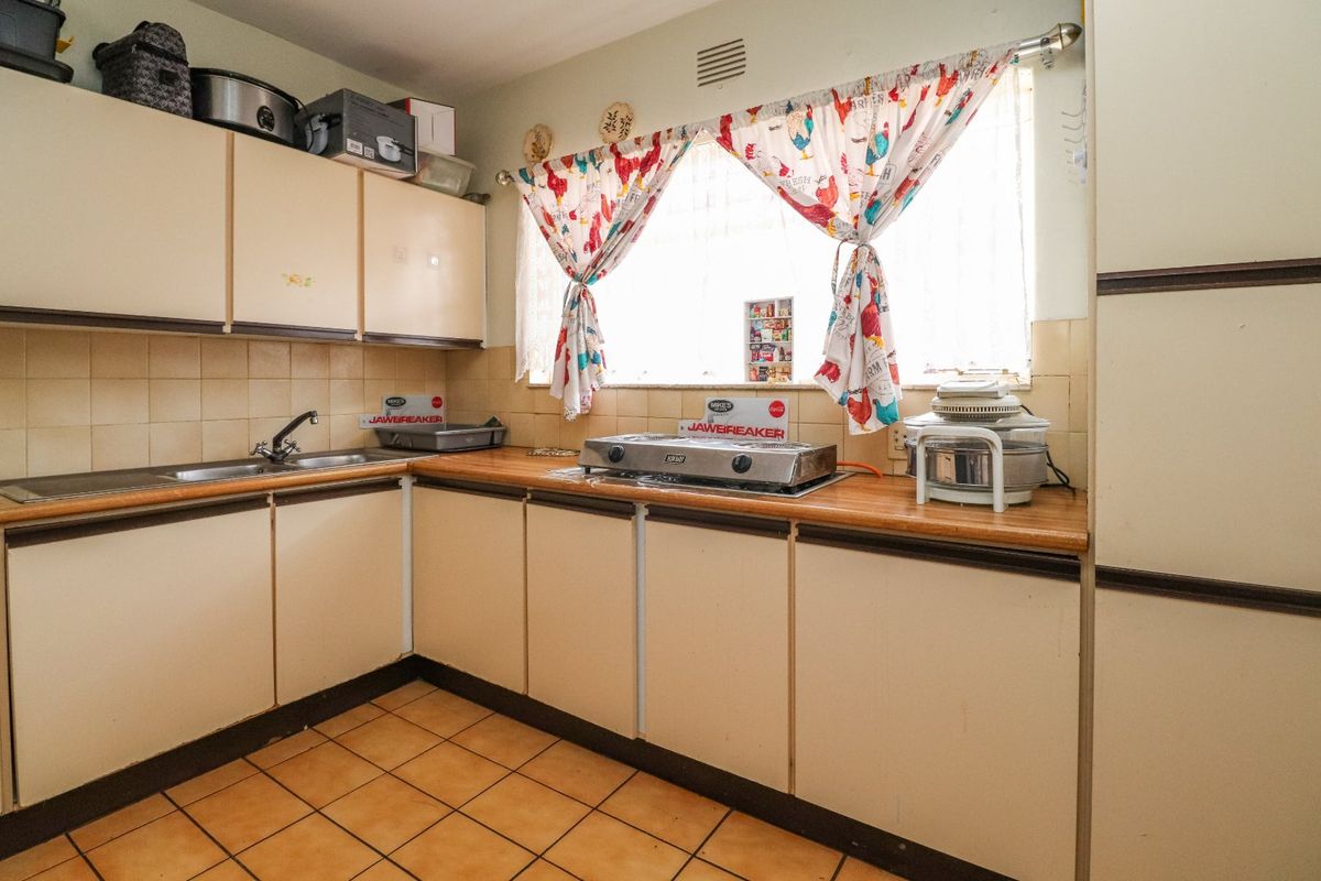 A functional kitchen featuring laminate countertops, tiled backsplash, built-in cabinetry, and ceramic floor tiles, offering potential for modernization.