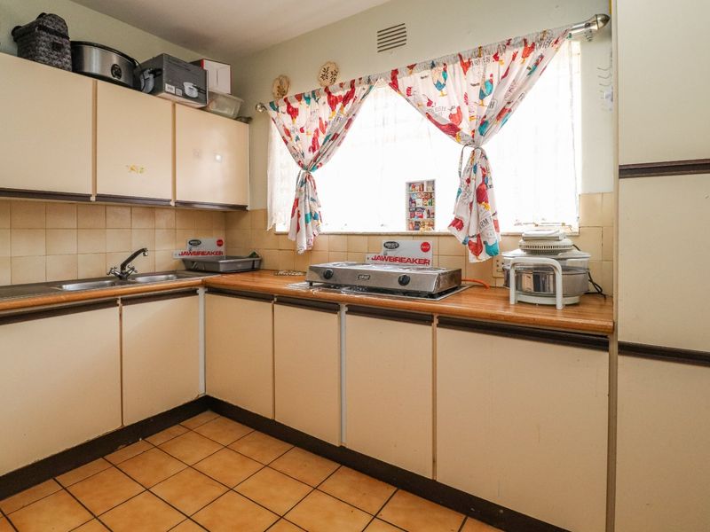 A functional kitchen featuring laminate countertops, tiled backsplash, built-in cabinetry, and ceramic floor tiles, offering potential for modernization.