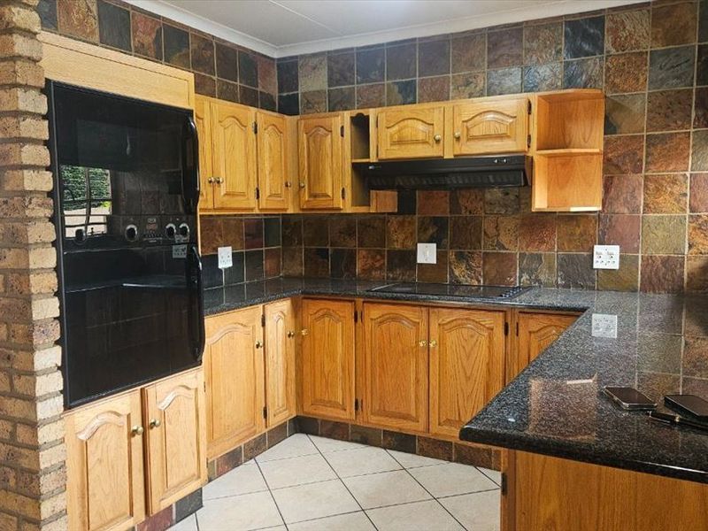 A functional kitchen featuring wooden cabinetry, granite countertops, a built-in oven, electric hob, and distinctive slate tile backsplash with an exposed brick feature.