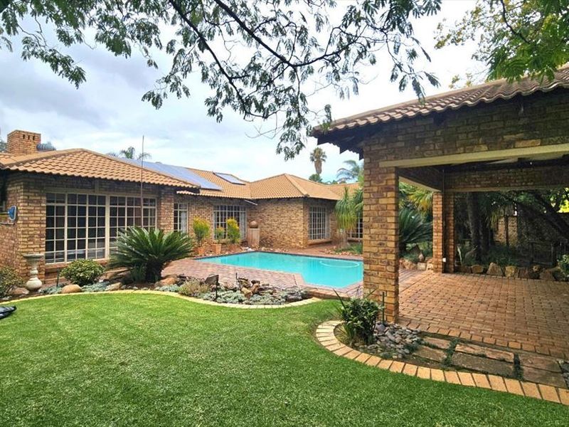 Spacious rear garden featuring a swimming pool, covered brick patio, and well-maintained lawn, complemented by a classic face brick house exterior.