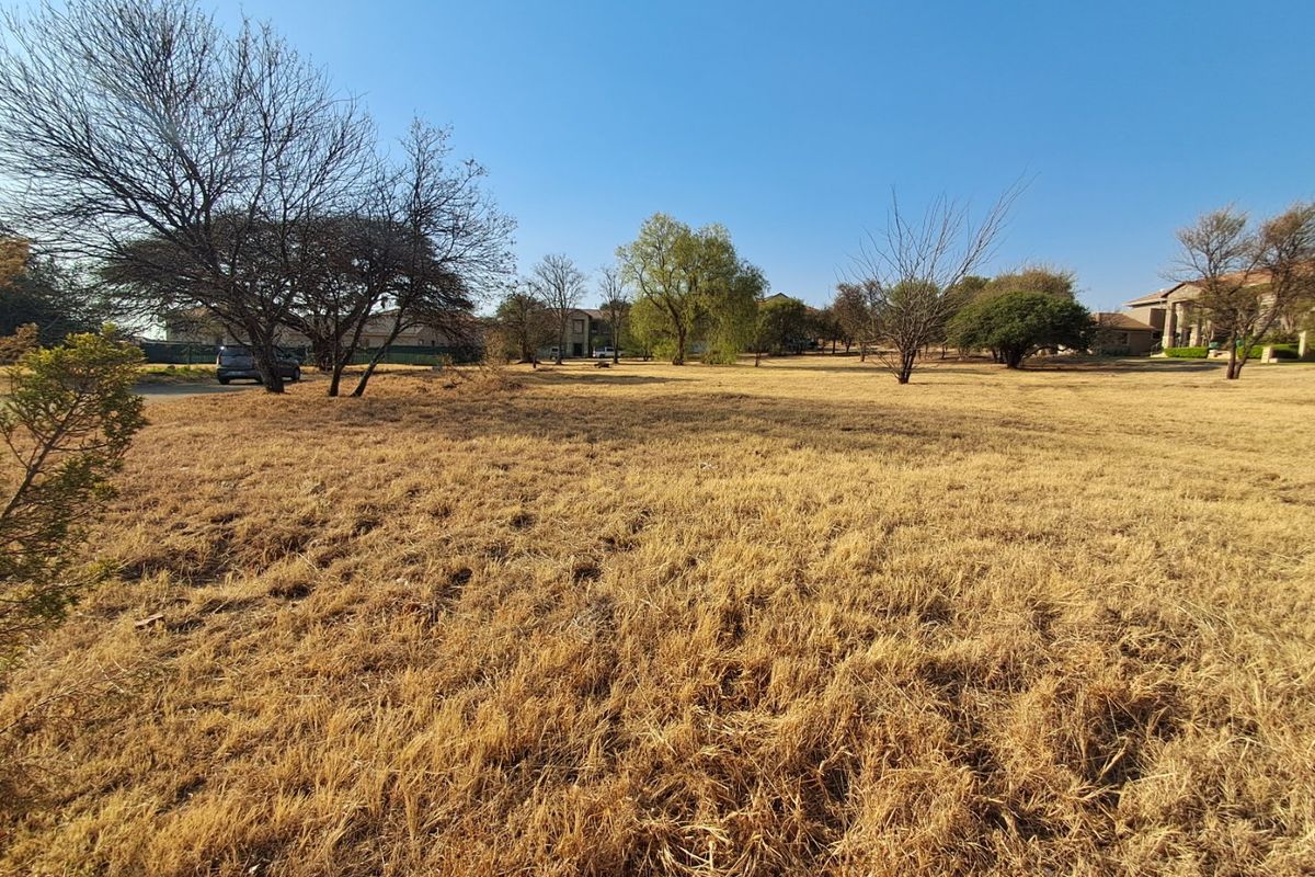 A wide-angle view of a vacant residential plot featuring established trees and dry grass, offering a blank canvas for future development.