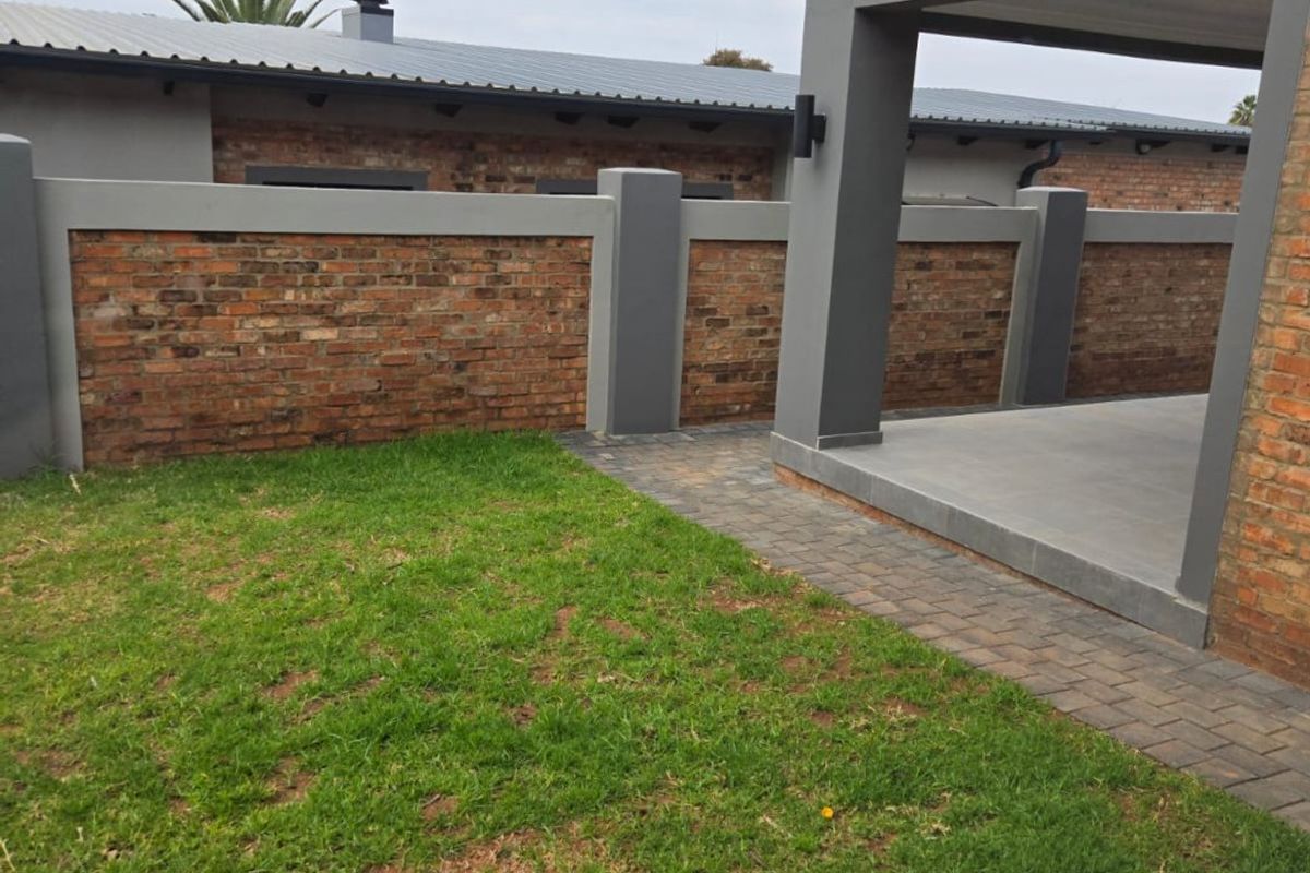 A well-maintained rear garden featuring a paved walkway, a covered patio area, and a brick boundary wall.
