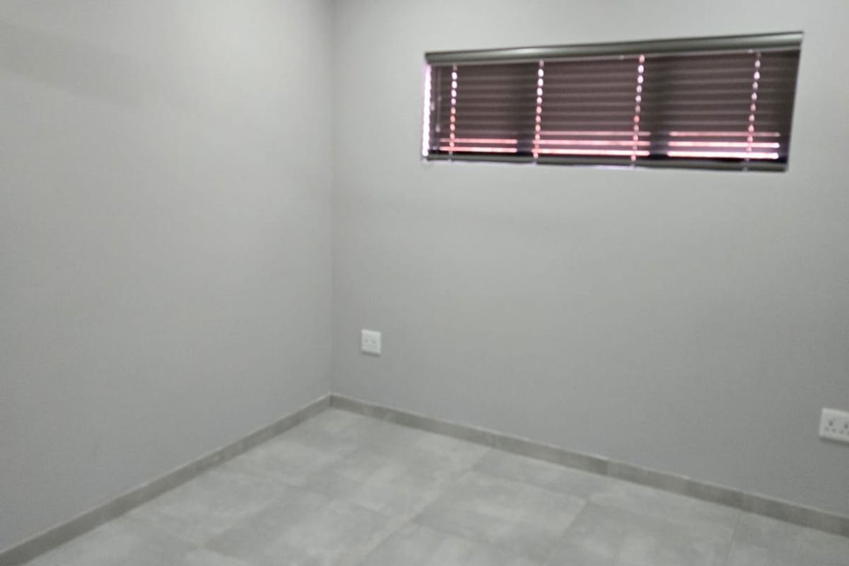 A clean, modern, and empty bedroom featuring neutral grey tiled flooring, a ceiling fan, recessed lighting, and fitted venetian blinds.