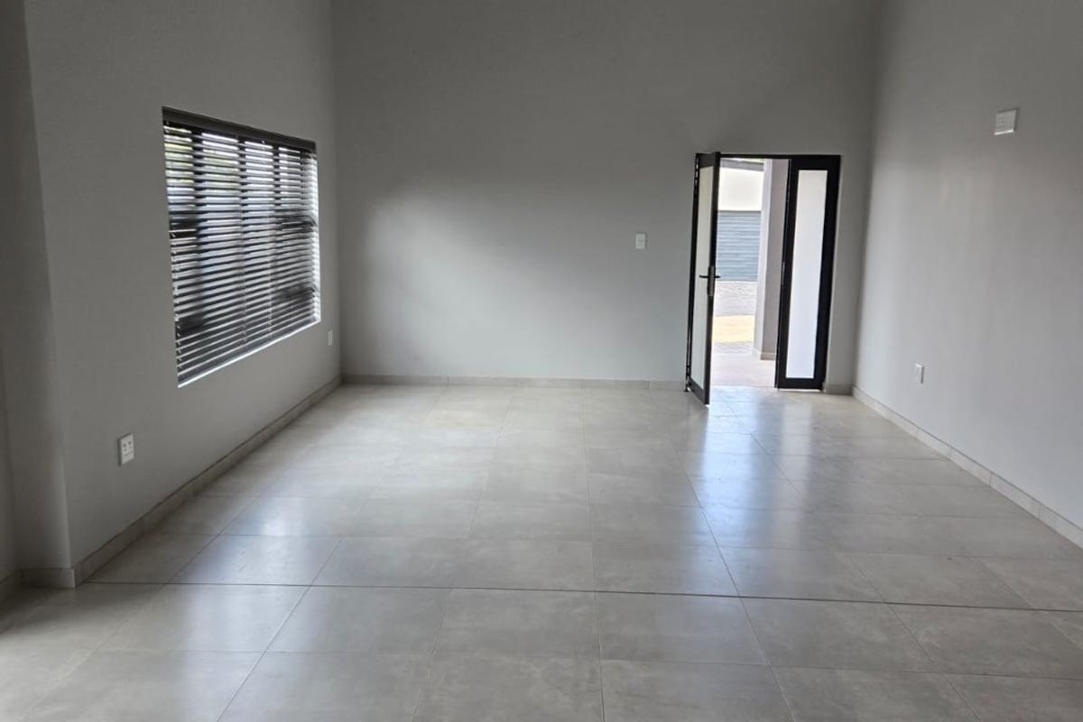 Spacious, light-filled living area featuring modern large-format floor tiles, exposed timber ceiling beams, and neutral wall finishes.