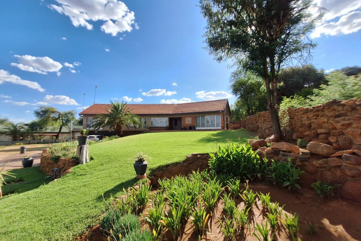 A well-maintained rear garden featuring a terraced stone retaining wall, expansive lawn, and a single-story residence with a tiled roof and sliding glass doors.