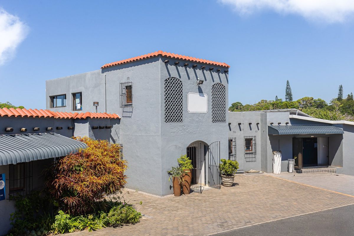Front exterior view of a commercial building featuring Mediterranean-style architecture with stucco walls, terracotta roof tiles, and paved driveway access.