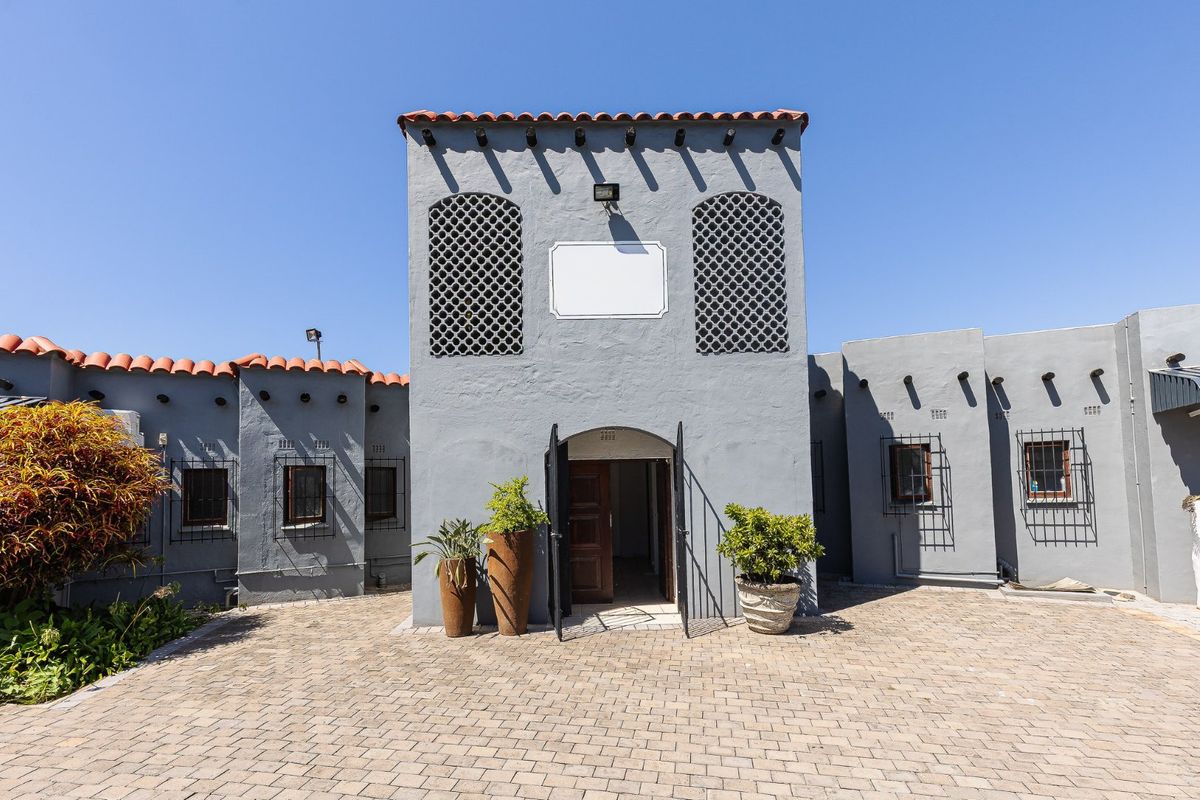 Front facade of a commercial building featuring grey stucco walls, terracotta roof tiles, decorative lattice screens, and a paved entrance courtyard.