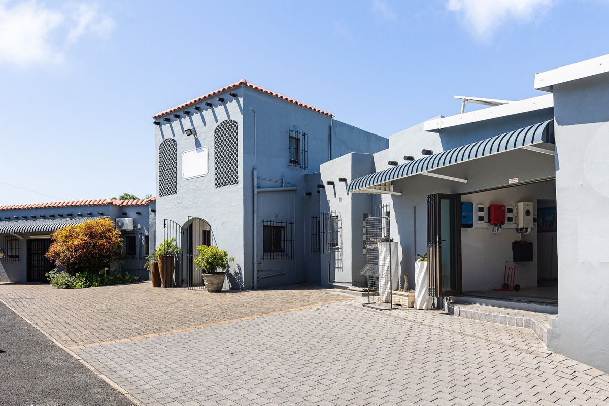 Front exterior view of a commercial property featuring paved driveway, security features, and an external solar power installation.