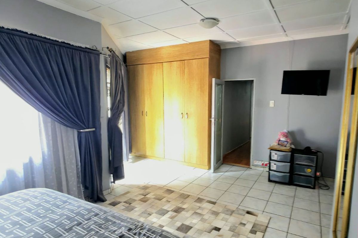 A bedroom featuring tiled flooring, built-in wooden cupboards, and a drop ceiling, providing a functional space with potential for cosmetic updates.