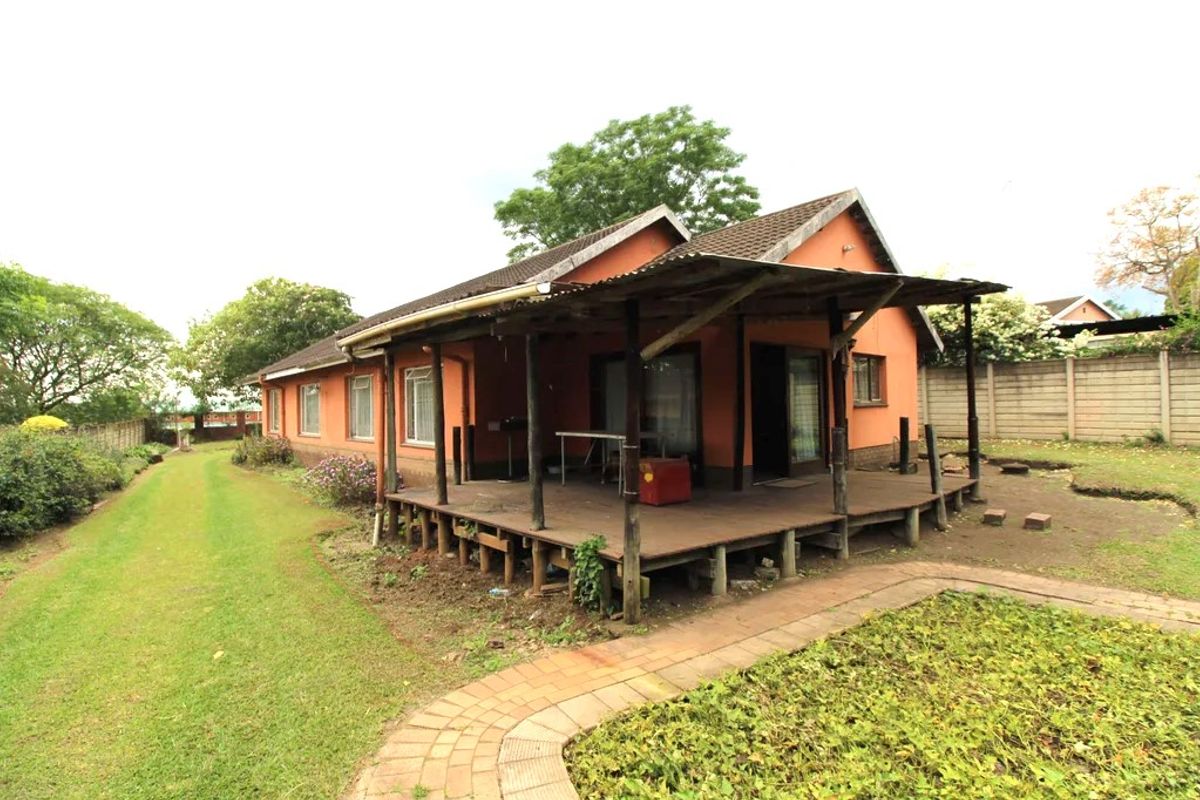 Rear view of the property featuring a raised timber deck with a corrugated iron roof, overlooking a spacious garden with brick paved pathways.