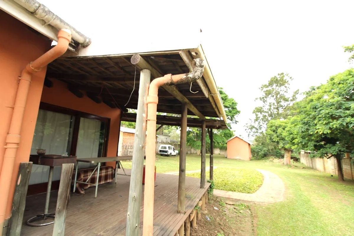 A covered timber patio overlooking a spacious rear garden, featuring exposed rafters and requiring maintenance to the guttering and decking surfaces.