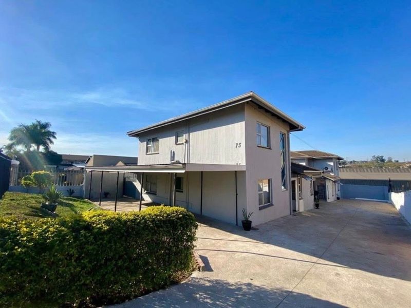 A well-maintained two-story residential property featuring a paved driveway, attached carport, and landscaped garden area.