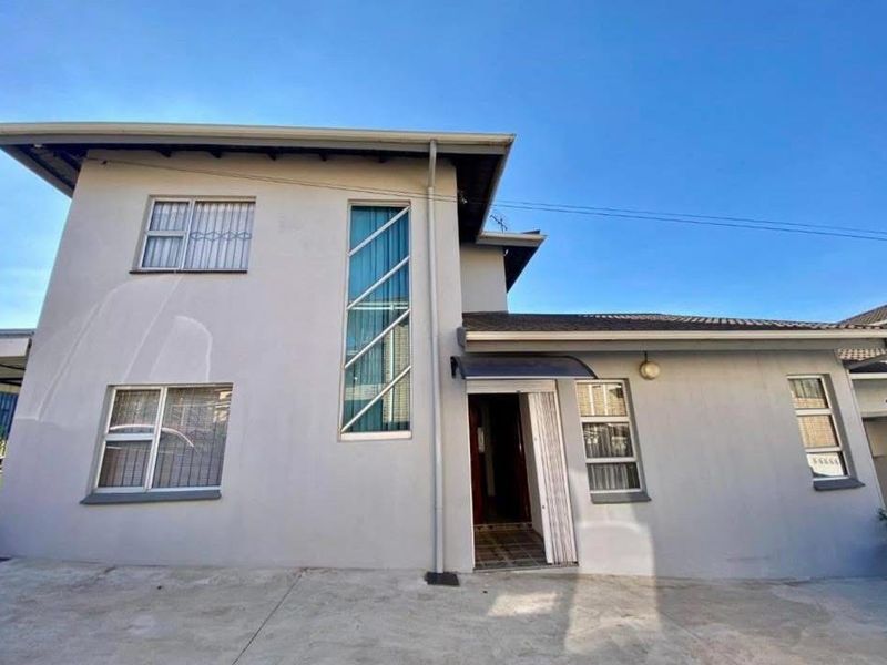 Front elevation of a two-story house featuring a concrete driveway, security bars on windows, and a distinctive vertical feature window.