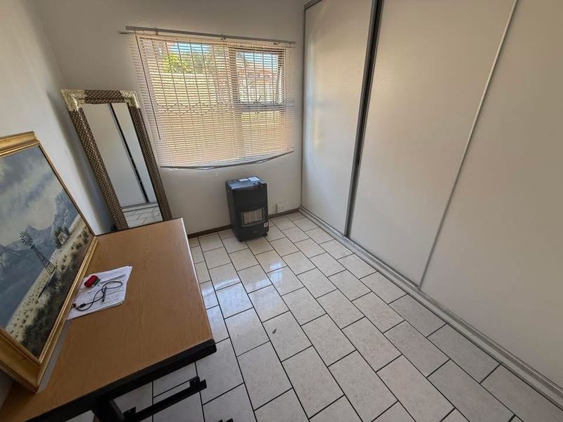 A bedroom featuring tiled flooring, a built-in sliding door wardrobe, and a window with fitted blinds.
