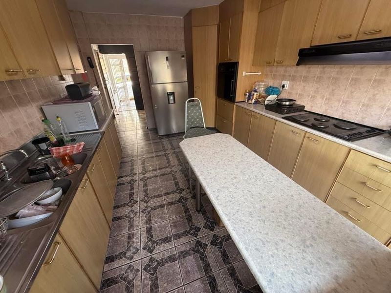 A functional kitchen featuring laminate cabinetry, built-in oven, extractor fan, and tiled finishes, offering a practical layout with potential for modern updates.