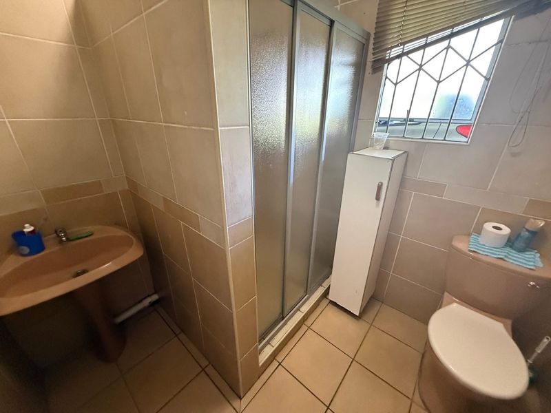 A functional bathroom featuring a pedestal basin, shower enclosure, and toilet, finished with neutral wall and floor tiling.