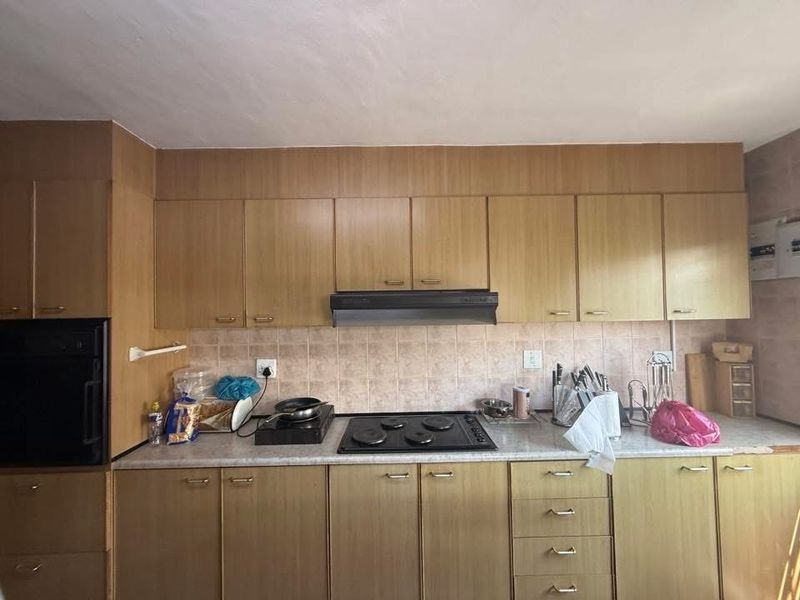 A functional kitchen featuring wood-look laminate cabinetry, a built-in oven, electric hob, extractor fan, and tiled backsplash.