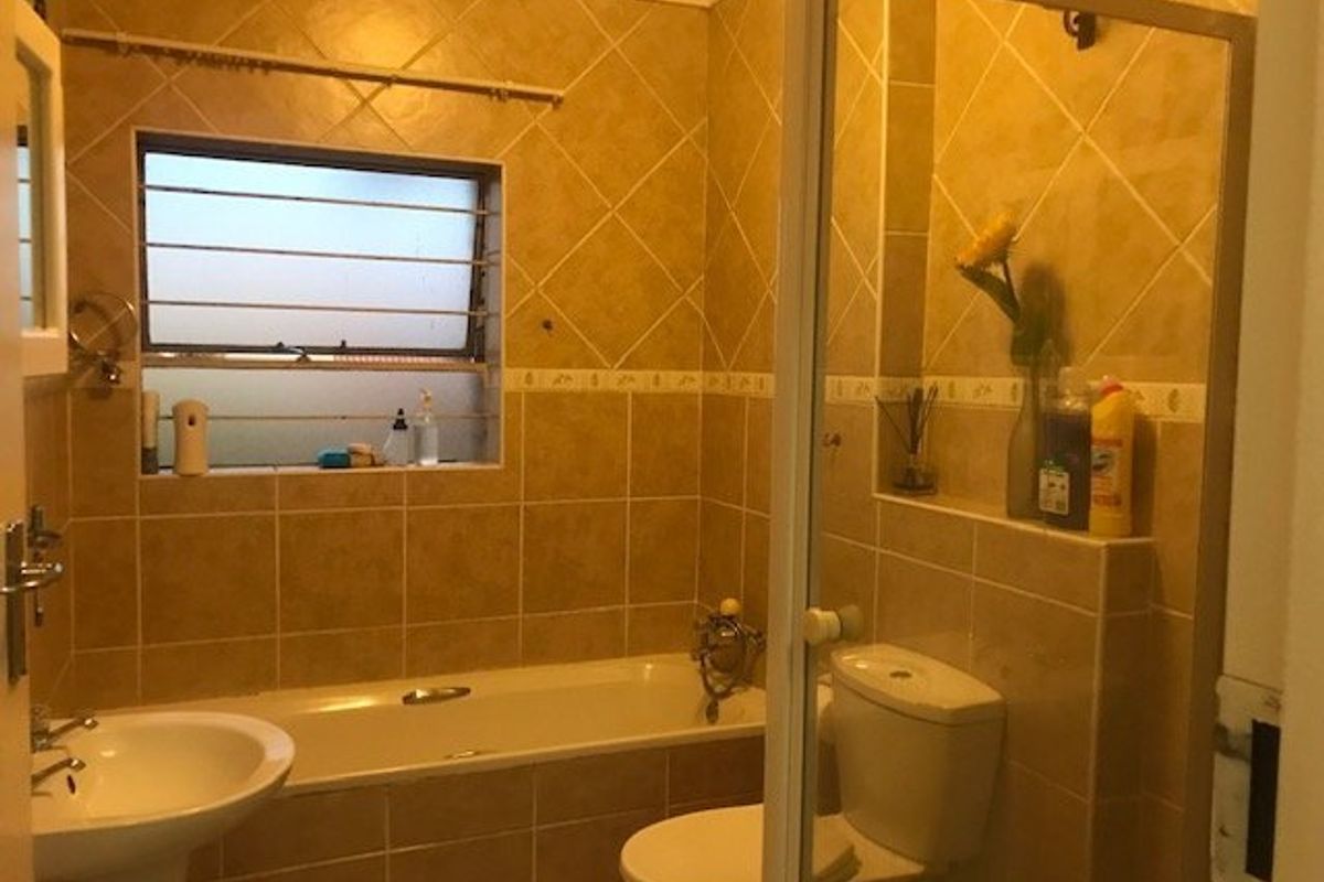 A functional bathroom featuring a pedestal basin, bathtub, and a separate shower enclosure with tiled walls and a louvered window.