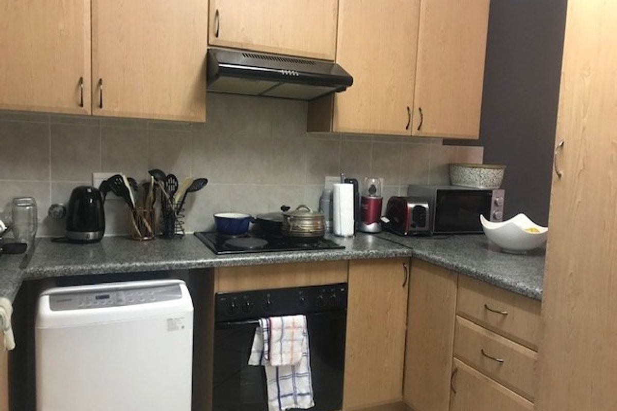A functional kitchen featuring light wood-finish cabinetry, granite-look countertops, a tiled backsplash, and built-in cooking appliances.