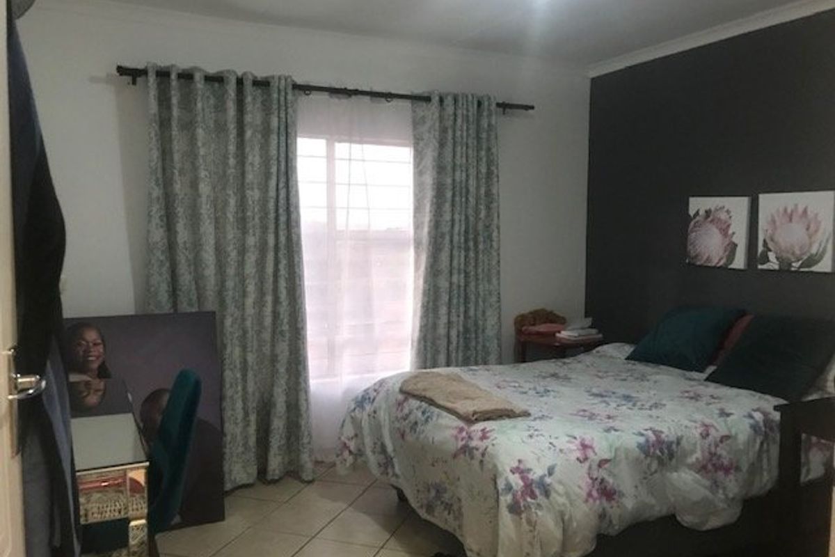 A bedroom featuring tiled flooring and a window with security bars, providing a functional space with a neutral and dark accent wall.