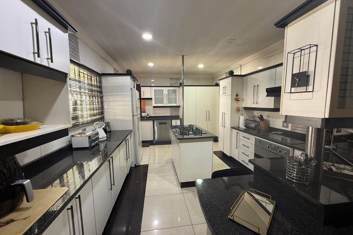 Modern kitchen featuring high-contrast black and white cabinetry, granite countertops, a central island with a gas hob, and integrated appliances.