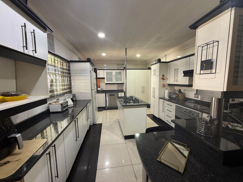 Modern kitchen featuring high-contrast black and white cabinetry, granite countertops, a central island with a gas hob, and integrated appliances.