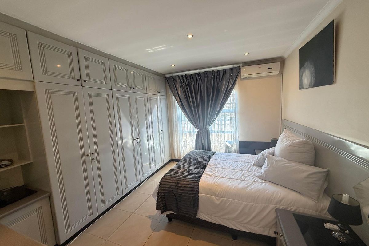 A well-maintained bedroom featuring extensive built-in cabinetry, tiled flooring, recessed lighting, and a wall-mounted split-system air conditioner.