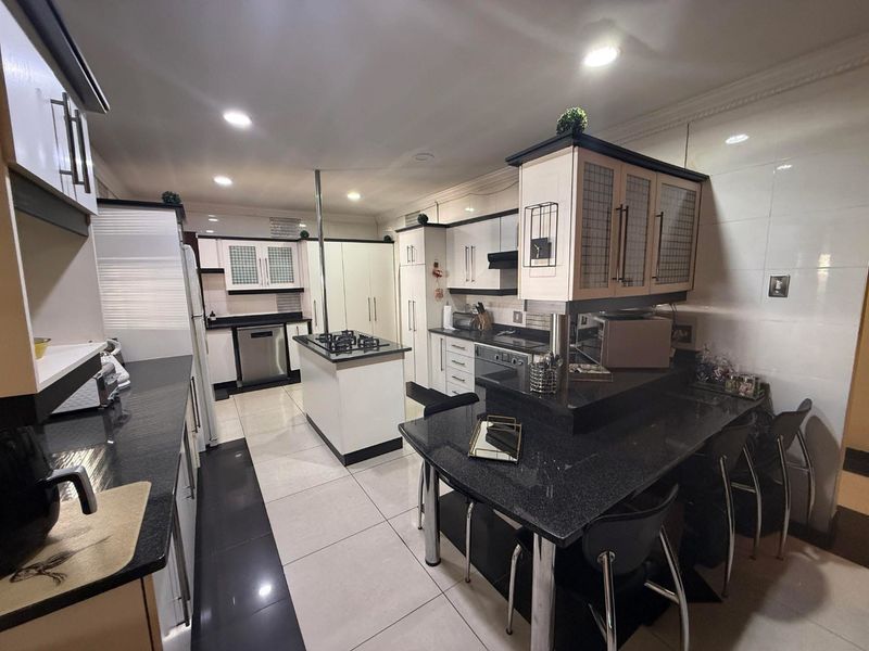 A well-appointed kitchen featuring black granite countertops, a central island with a gas hob, integrated cabinetry, and modern tiled flooring.