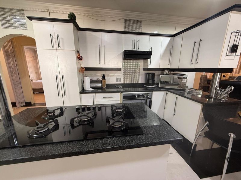 A functional kitchen featuring white cabinetry, dark granite countertops, a central island with a gas hob, and integrated appliances.