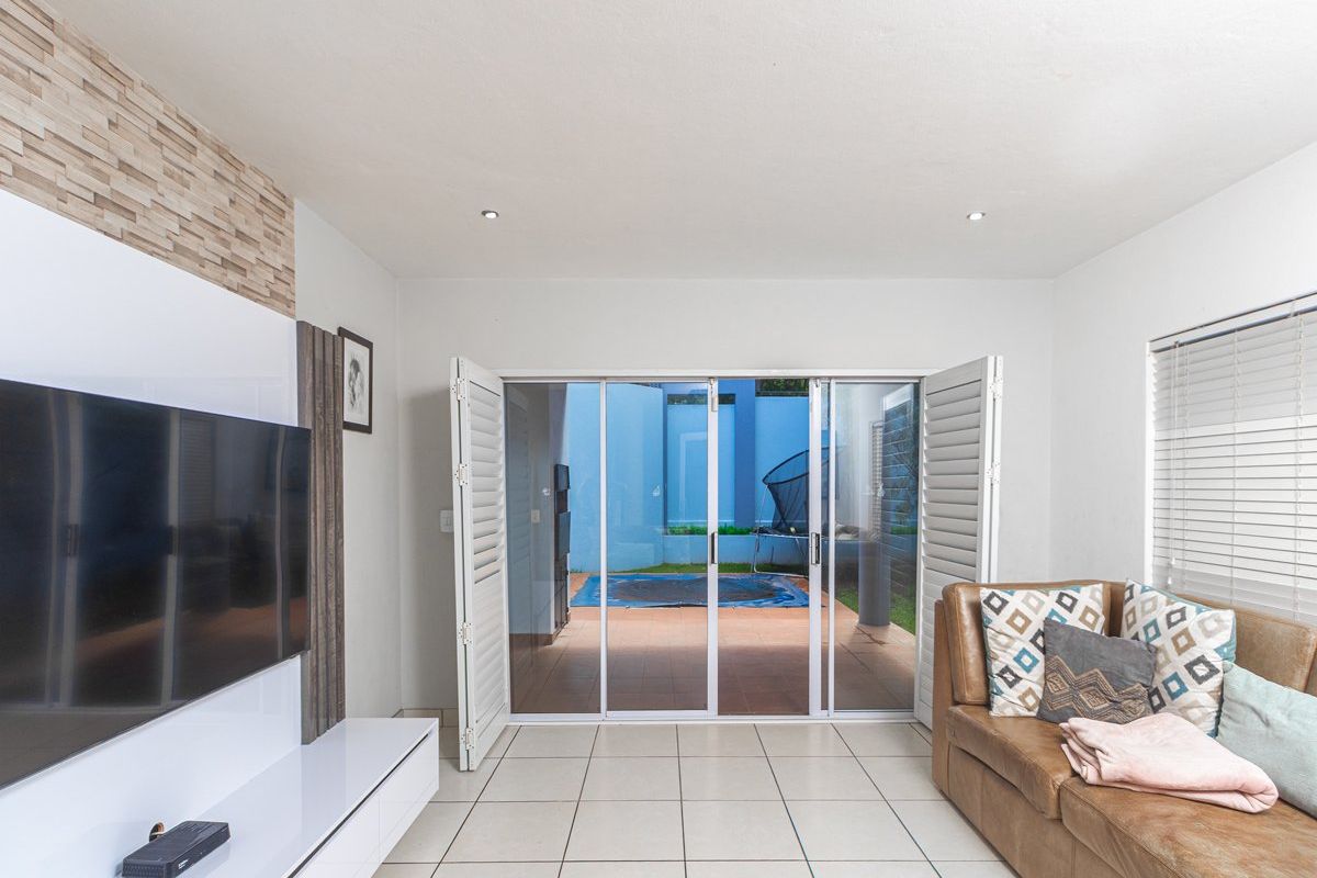 A bright living room featuring tiled flooring, a built-in media unit, and folding doors that open directly onto a patio and pool area.