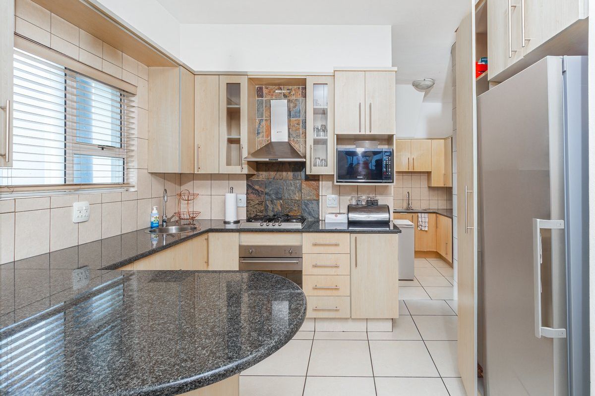 A functional kitchen featuring granite countertops, light wood cabinetry, a built-in oven, gas hob, extractor fan, and an adjoining scullery area.