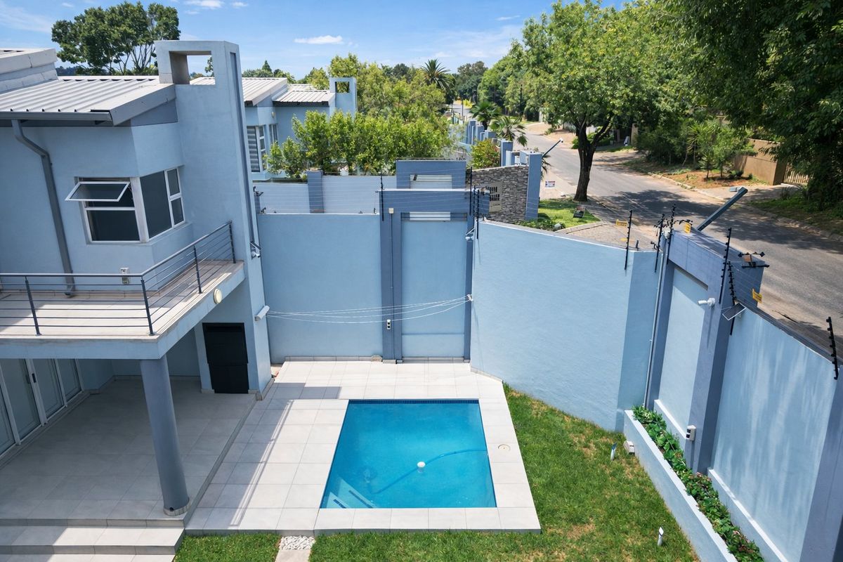 Aerial view of a modern residential backyard featuring a swimming pool, paved patio area, and perimeter wall with electric fencing.