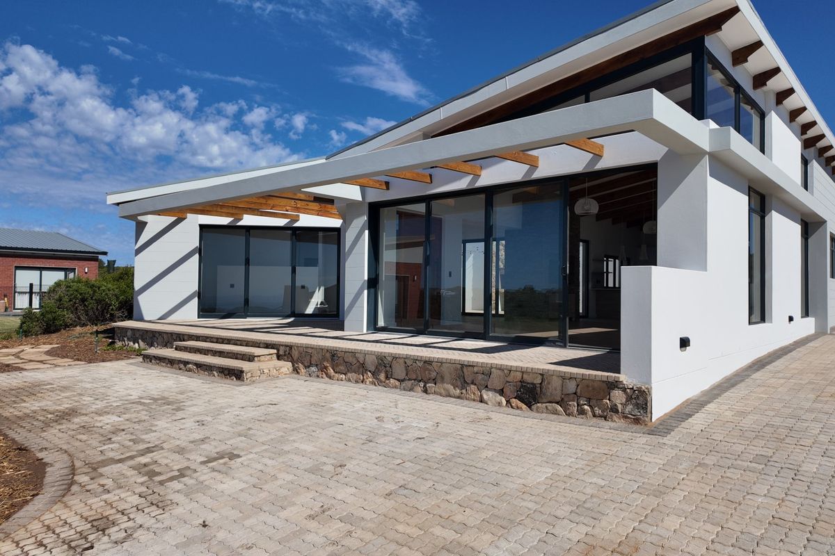 Modern rear elevation featuring a covered patio with exposed timber rafters, stone-clad masonry base, and large sliding glass doors opening to a paved area.
