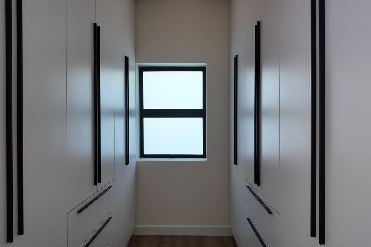 A modern walk-in closet or dressing area featuring floor-to-ceiling built-in cabinetry with sleek black handles and neutral finishes.