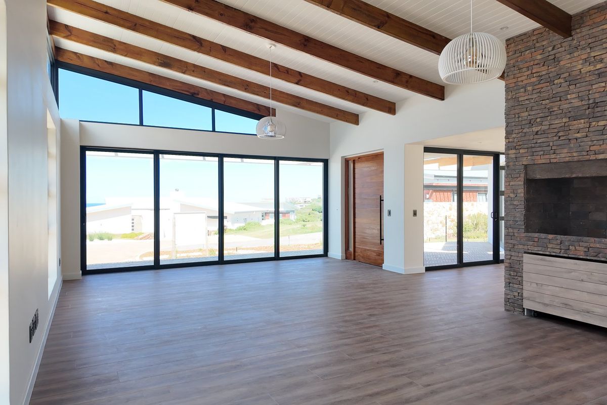 Spacious open-plan living area featuring exposed timber beams, a striking stone-clad fireplace, and expansive glass doors opening to the exterior.