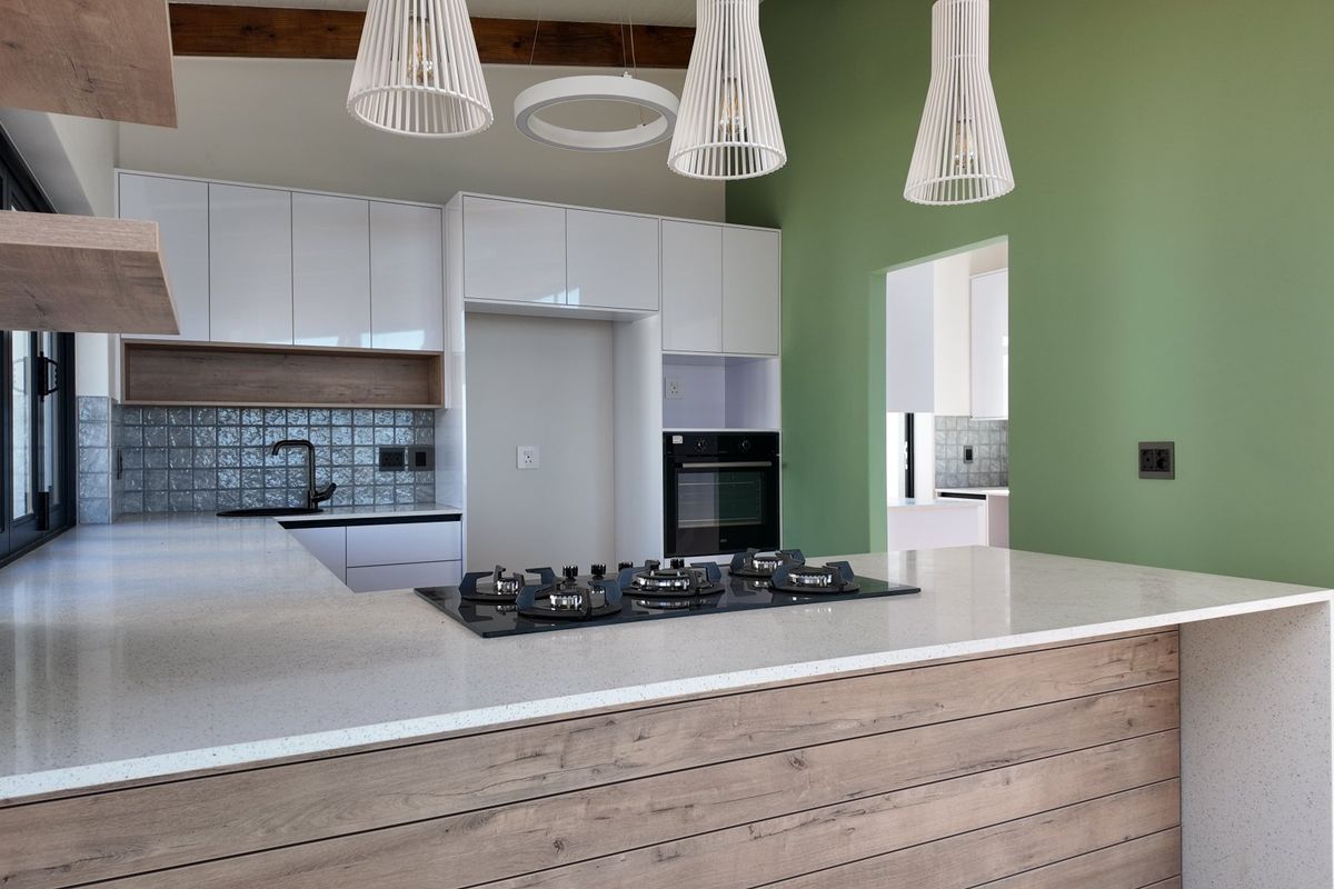Modern kitchen featuring a central island with a gas hob, sleek white cabinetry, quartz countertops, and a striking green accent wall.