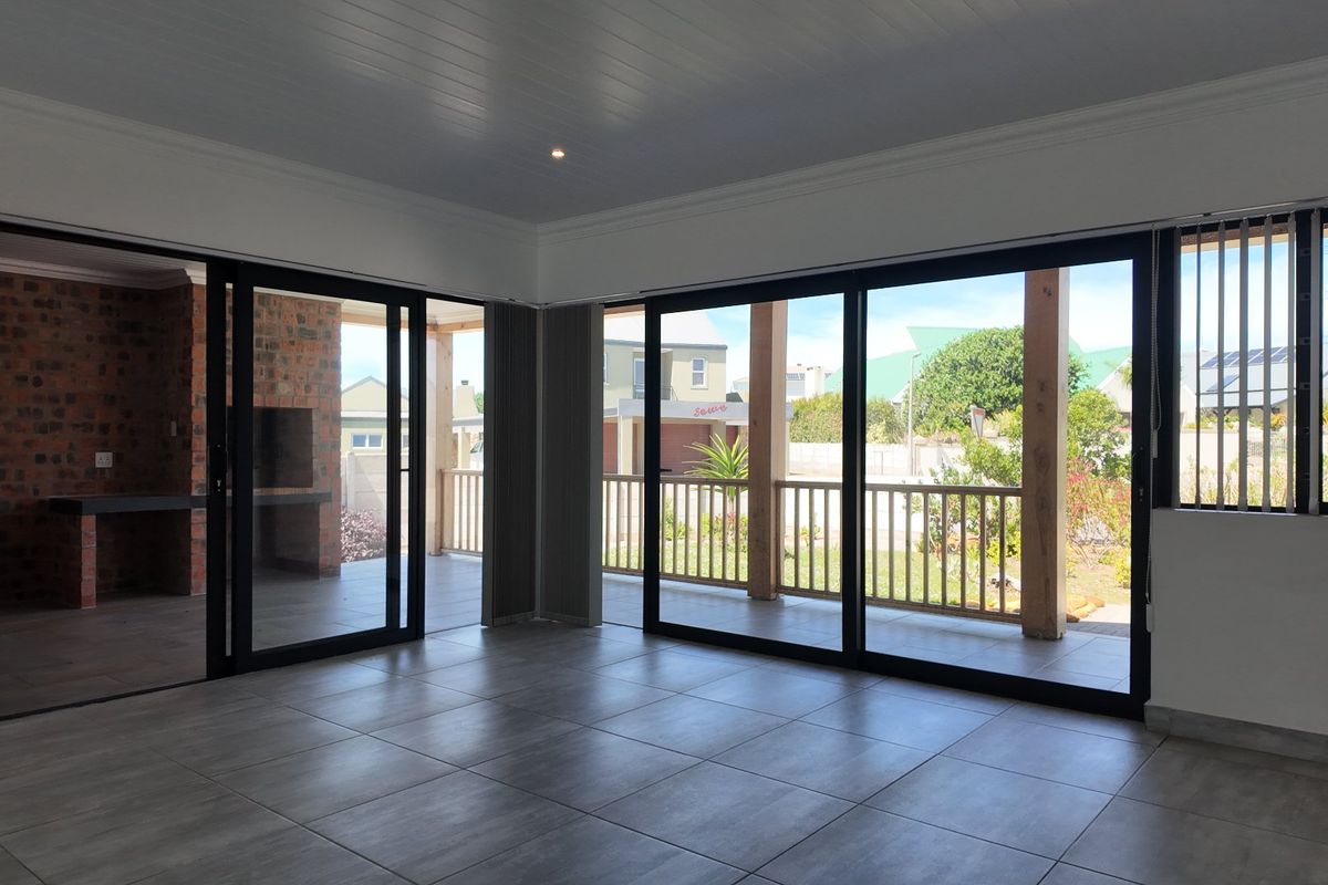 Spacious, light-filled living area featuring large sliding glass doors that open onto a covered patio with a built-in brick braai.