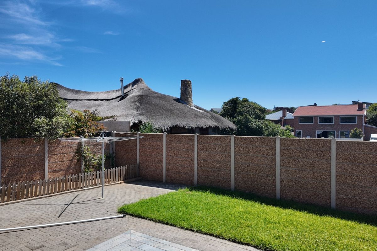 A rear garden area featuring a paved patio, a small lawn, and a precast concrete boundary wall.