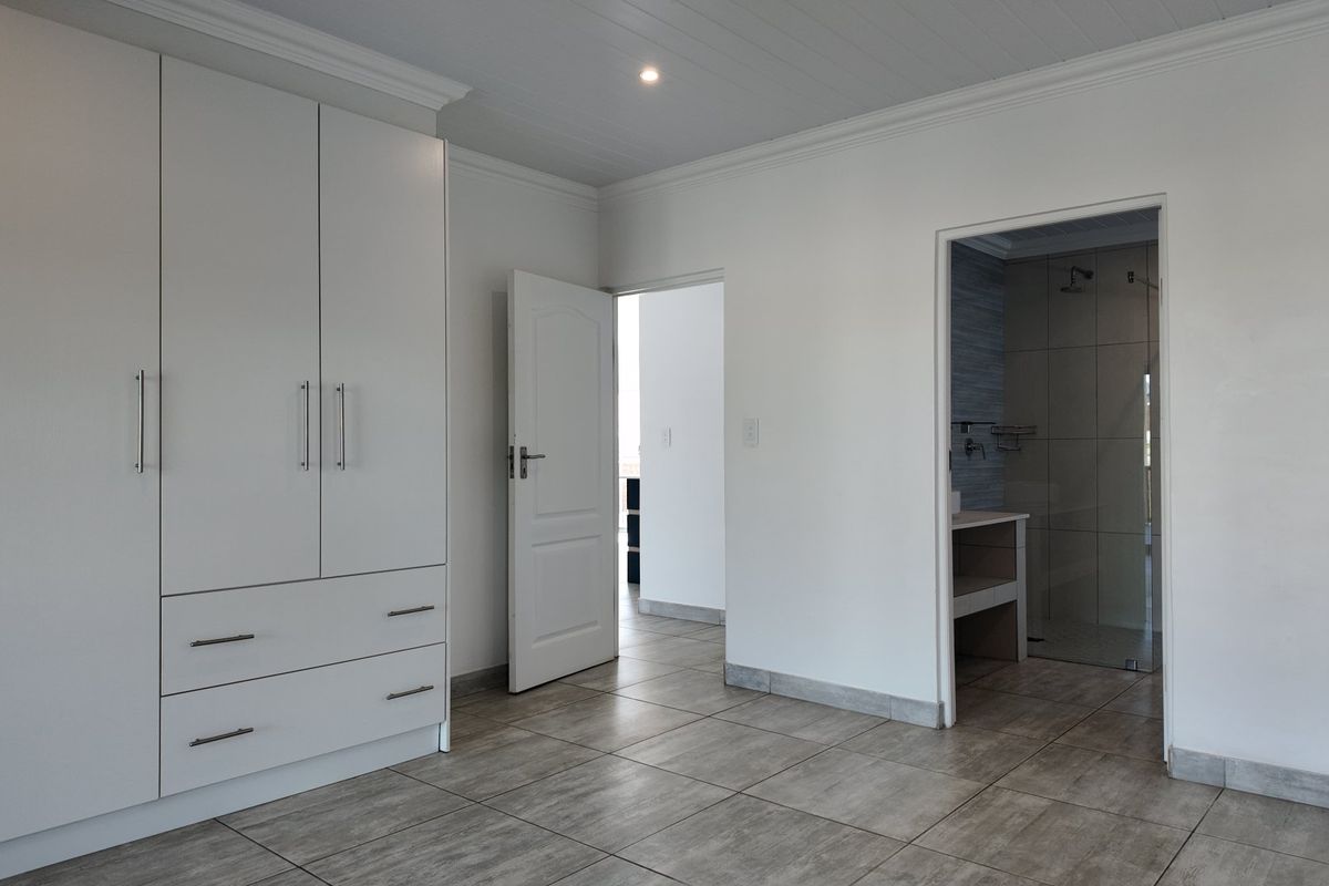 A clean, modern bedroom featuring neutral tiled flooring, ample built-in cupboard storage, and direct access to an en-suite bathroom.