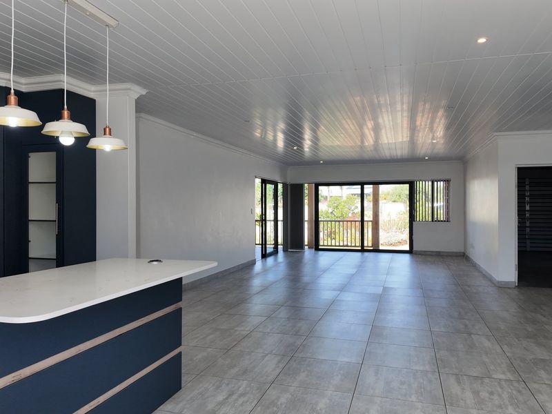 Spacious open-plan living area featuring modern tiled flooring, a sleek kitchen island with stone countertops, and large sliding doors leading to the outdoors.