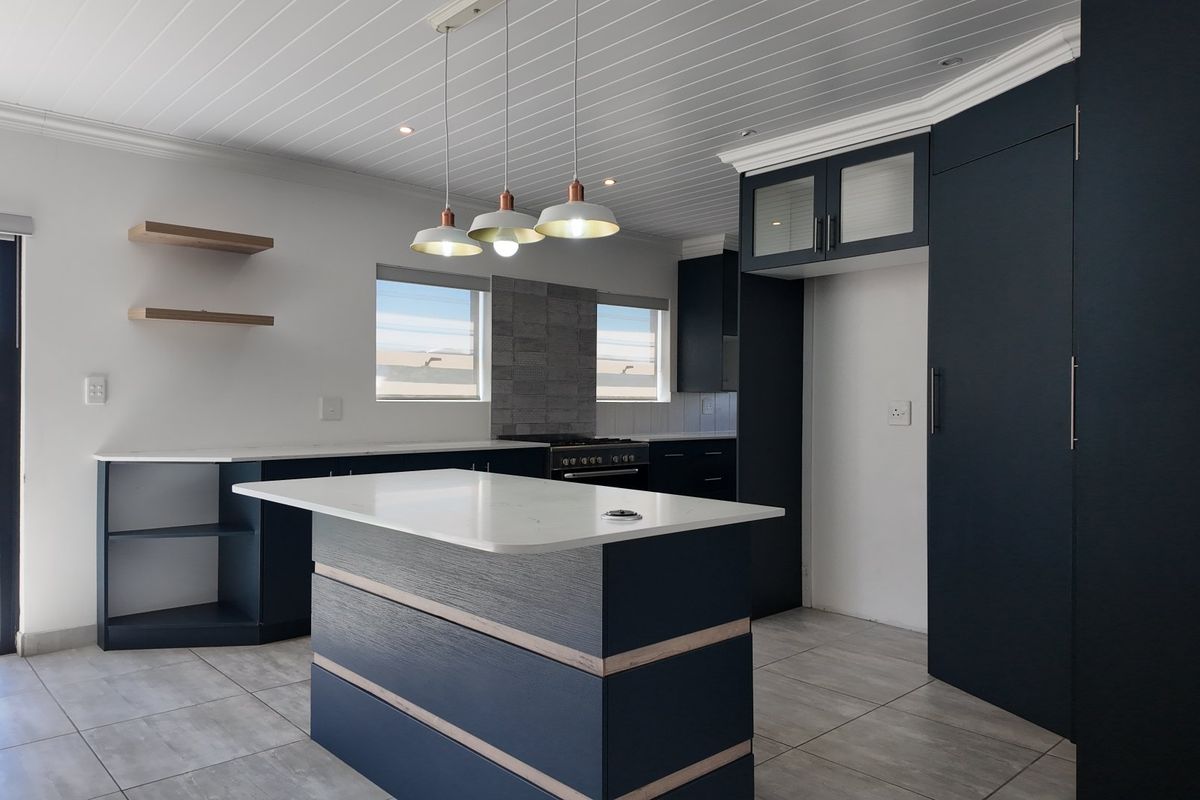 Modern kitchen featuring a central island with stone countertops, dark cabinetry, gas stove, and tiled flooring, offering a clean and contemporary aesthetic.