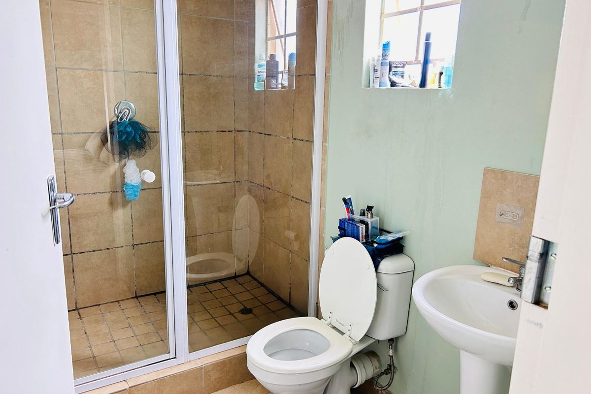 A functional bathroom featuring a shower enclosure, pedestal basin, and toilet, with tiled flooring and shower walls.