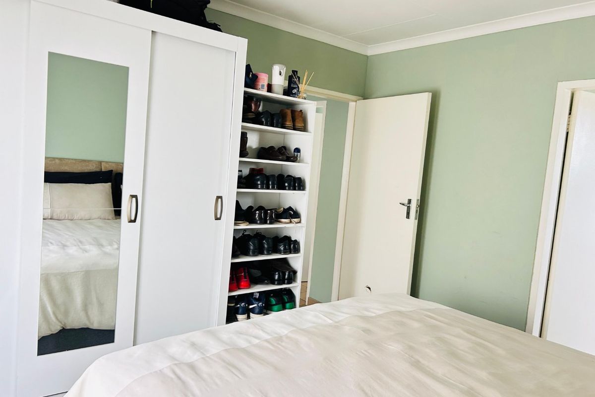 A bedroom featuring a built-in wardrobe with mirrored doors and sage green wall finishes.