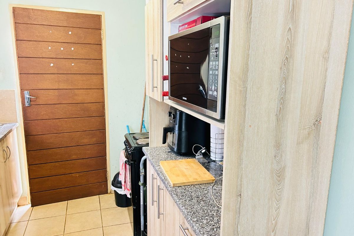 A functional kitchen area featuring light wood-finish cabinetry, granite countertops, a built-in microwave, and tiled flooring.