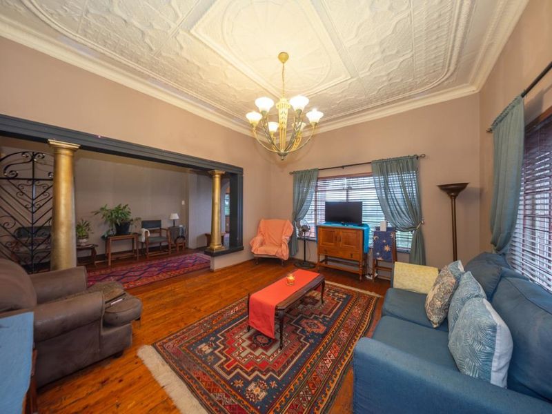Spacious living room featuring original pressed metal ceilings, polished hardwood floors, and a decorative archway with columns leading to an adjacent area.