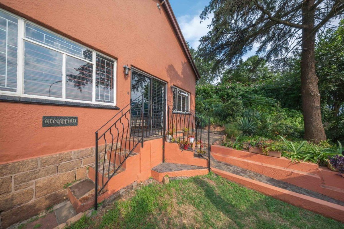 Rear exterior view of the house featuring a sliding glass door, stone masonry base, and wrought iron railings leading to a garden area.