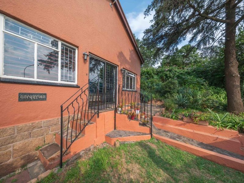 Rear exterior view of the house featuring a sliding glass door, stone masonry base, and wrought iron railings leading to a garden area.