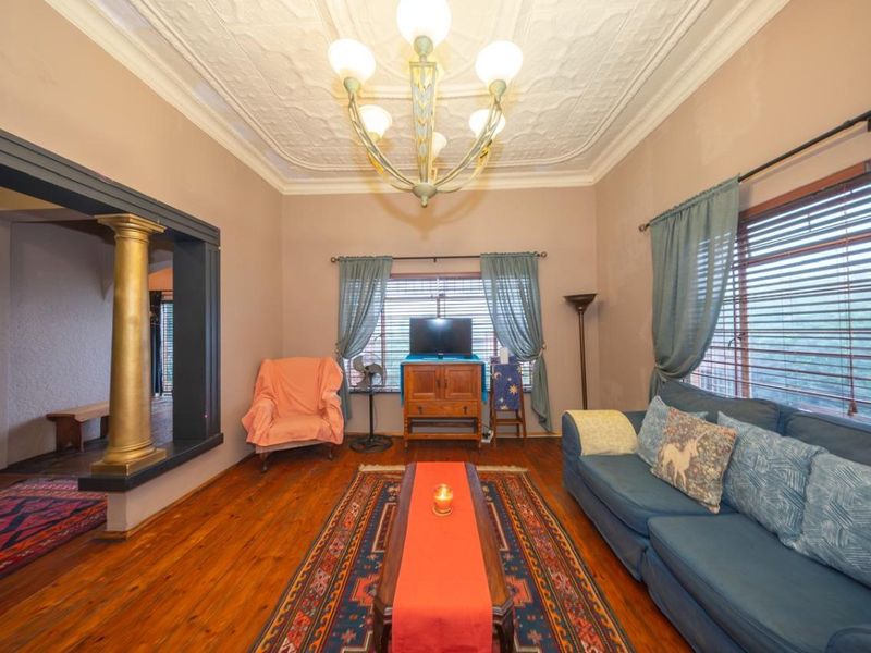 A living room featuring original hardwood flooring, a decorative pressed metal ceiling, and a classic column detail, offering a character-filled space with potential.