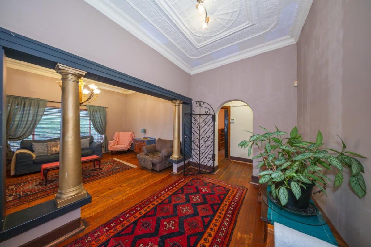 Spacious living area featuring original ornate plaster ceilings, decorative columns, hardwood flooring, and an arched doorway leading to adjacent rooms.