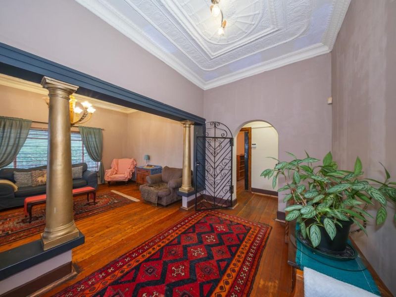 Spacious living area featuring original ornate plaster ceilings, decorative columns, hardwood flooring, and an arched doorway leading to adjacent rooms.